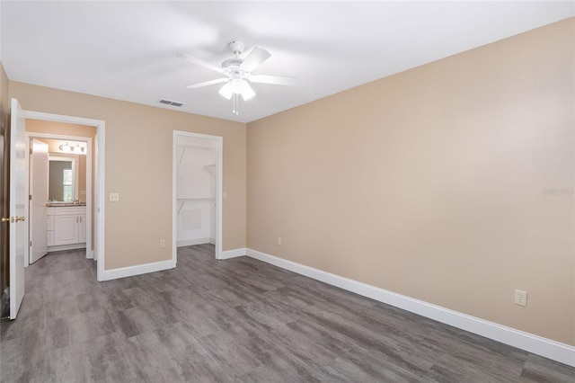 unfurnished bedroom featuring hardwood / wood-style floors, ceiling fan, a walk in closet, and a closet