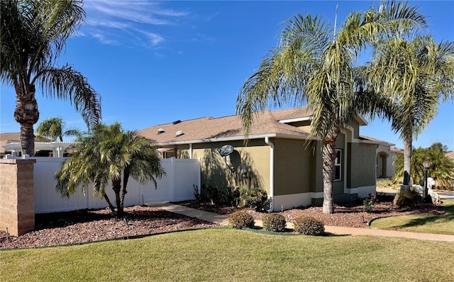 view of side of property featuring fence, a lawn, and stucco siding