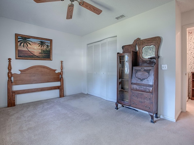 bedroom featuring ceiling fan, light colored carpet, a closet, and a textured ceiling