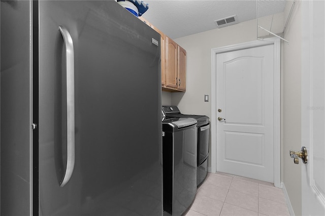 clothes washing area featuring washer and dryer, light tile patterned floors, cabinets, and a textured ceiling