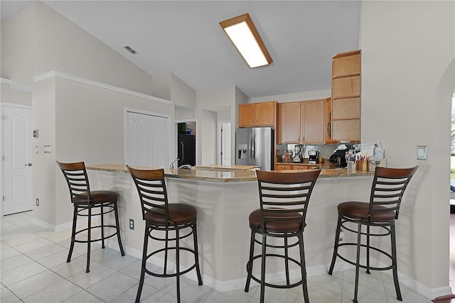 kitchen featuring lofted ceiling, stainless steel fridge, kitchen peninsula, and a breakfast bar