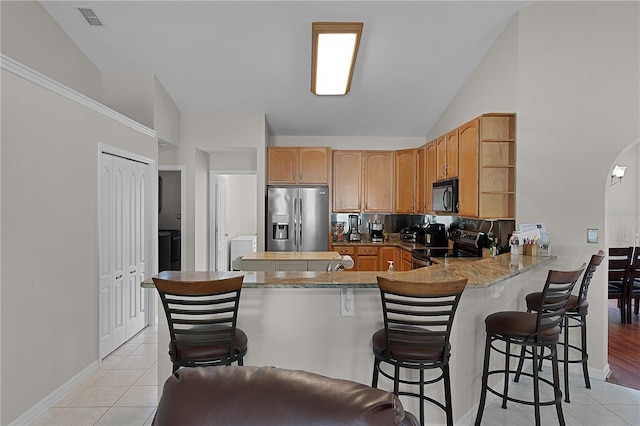 kitchen with light tile patterned flooring, appliances with stainless steel finishes, a kitchen breakfast bar, and kitchen peninsula