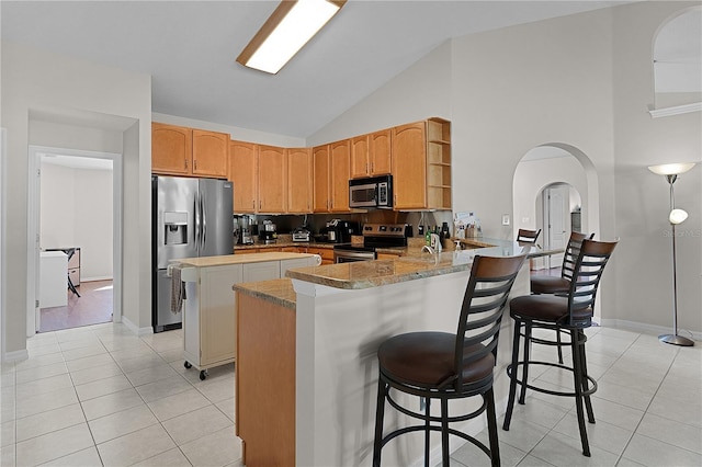 kitchen featuring a breakfast bar area, high vaulted ceiling, light tile patterned floors, kitchen peninsula, and stainless steel appliances