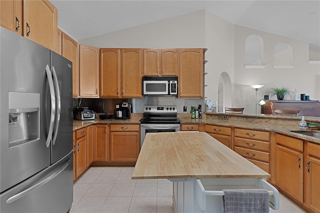 kitchen with lofted ceiling, butcher block countertops, appliances with stainless steel finishes, light tile patterned flooring, and decorative backsplash