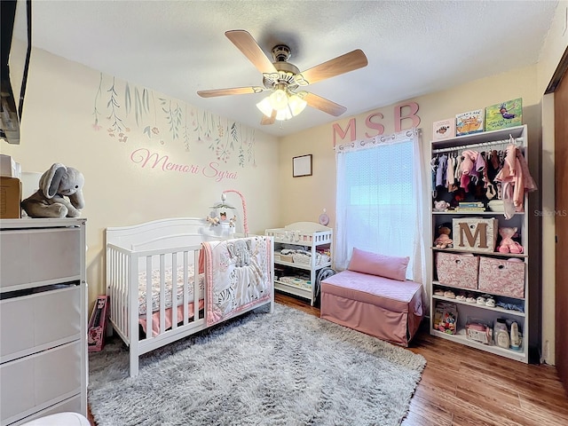 bedroom featuring hardwood / wood-style flooring, ceiling fan, a textured ceiling, a nursery area, and a closet