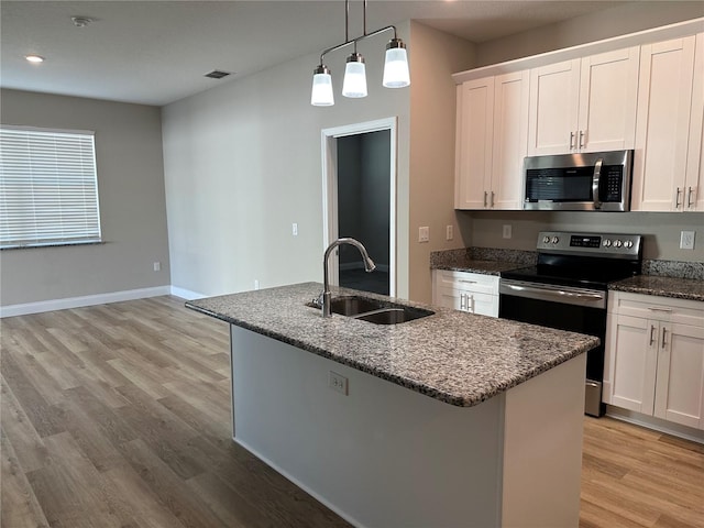 kitchen featuring sink, dark stone countertops, appliances with stainless steel finishes, an island with sink, and white cabinets