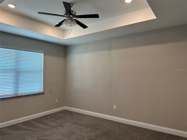 carpeted empty room with a raised ceiling and ceiling fan