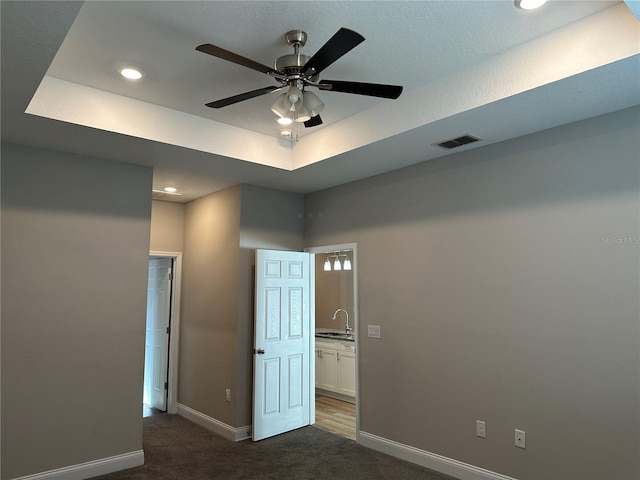 unfurnished bedroom featuring sink, a tray ceiling, ceiling fan, and dark colored carpet