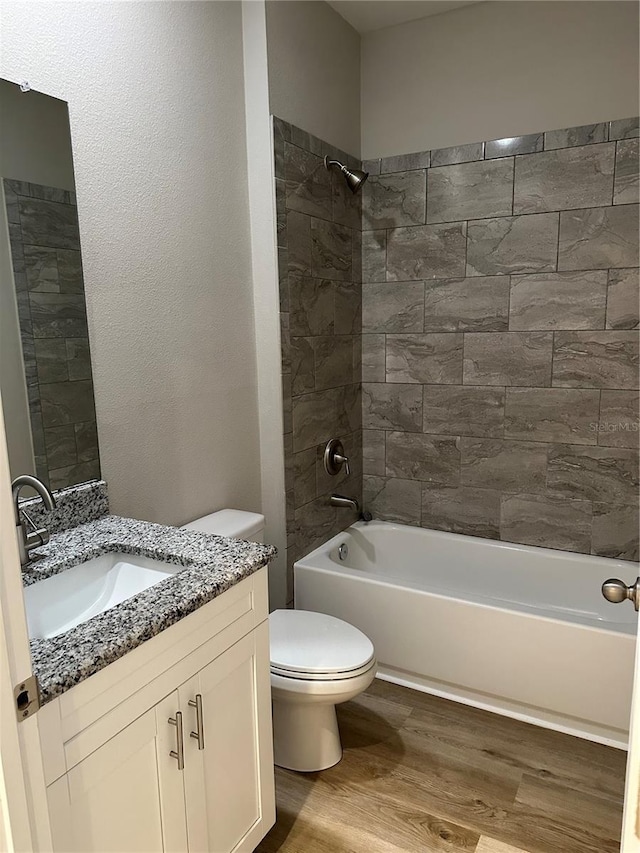 full bathroom with tiled shower / bath combo, vanity, hardwood / wood-style floors, and toilet