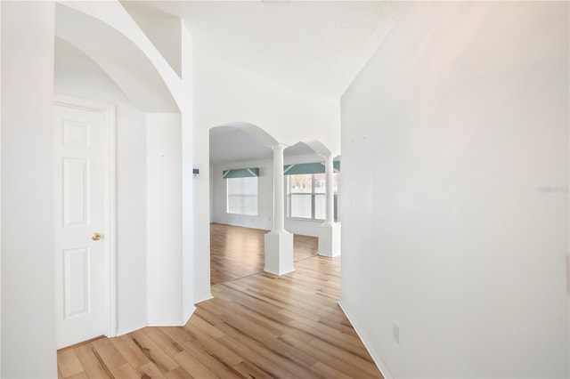 corridor featuring light hardwood / wood-style floors, lofted ceiling, and ornate columns