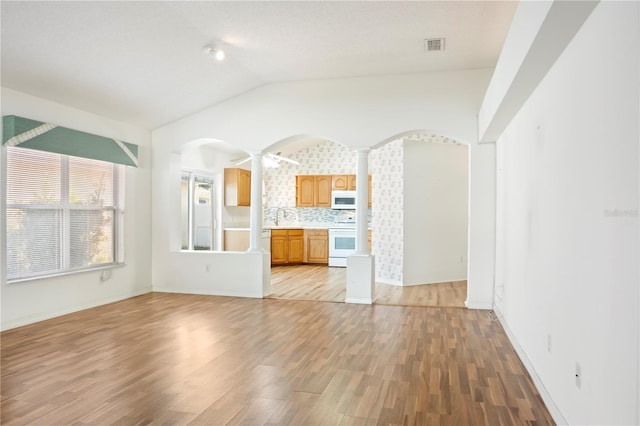 unfurnished living room featuring ornate columns, lofted ceiling, sink, and light hardwood / wood-style flooring