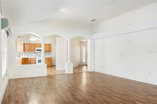 unfurnished living room featuring decorative columns, ceiling fan, lofted ceiling, and light wood-type flooring