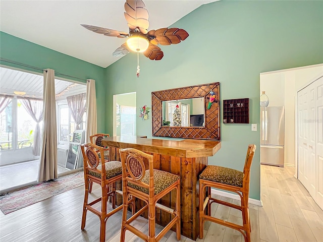 dining room with indoor bar, light wood-type flooring, ceiling fan, and lofted ceiling