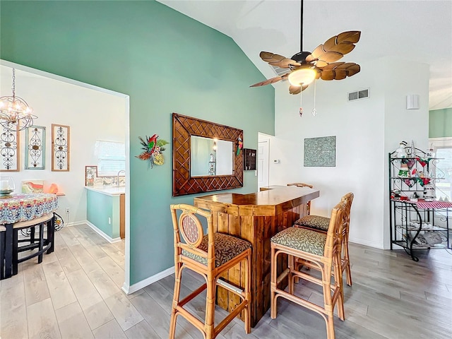 dining room featuring high vaulted ceiling, ceiling fan with notable chandelier, and light wood-type flooring