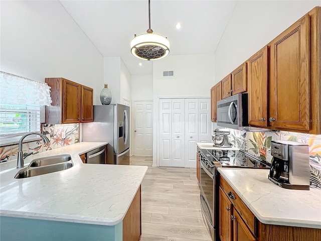 kitchen featuring appliances with stainless steel finishes, light stone counters, sink, pendant lighting, and light hardwood / wood-style flooring