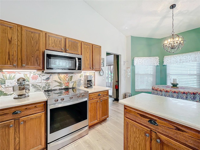 kitchen featuring pendant lighting, vaulted ceiling, a chandelier, appliances with stainless steel finishes, and light wood-type flooring