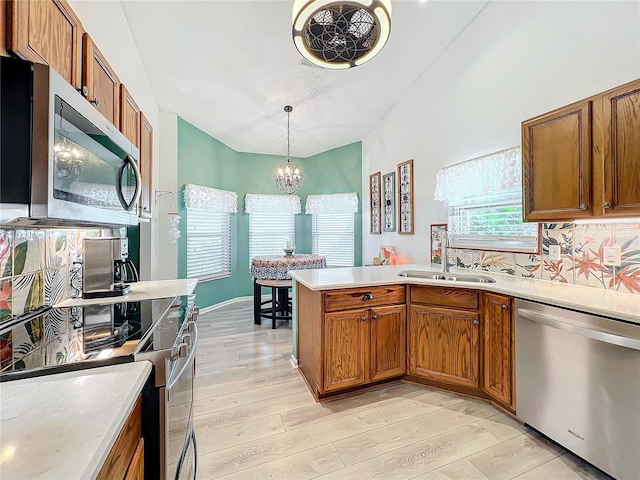 kitchen with light wood-type flooring, stainless steel appliances, sink, decorative light fixtures, and an inviting chandelier