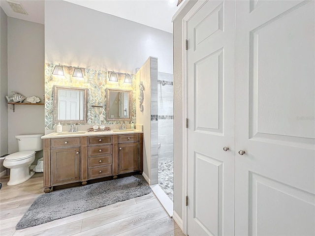 bathroom featuring vanity, toilet, wood-type flooring, and tiled shower