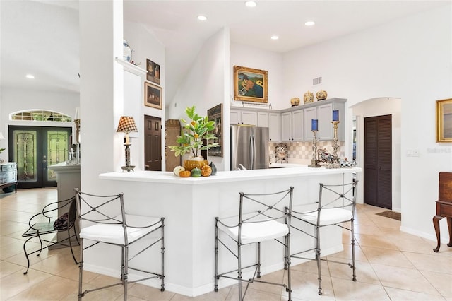 kitchen with kitchen peninsula, stainless steel fridge, a breakfast bar, light tile patterned floors, and gray cabinets