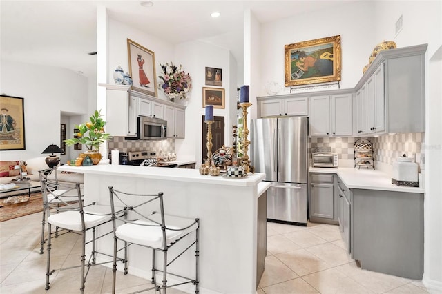 kitchen with a kitchen bar, appliances with stainless steel finishes, kitchen peninsula, and gray cabinetry