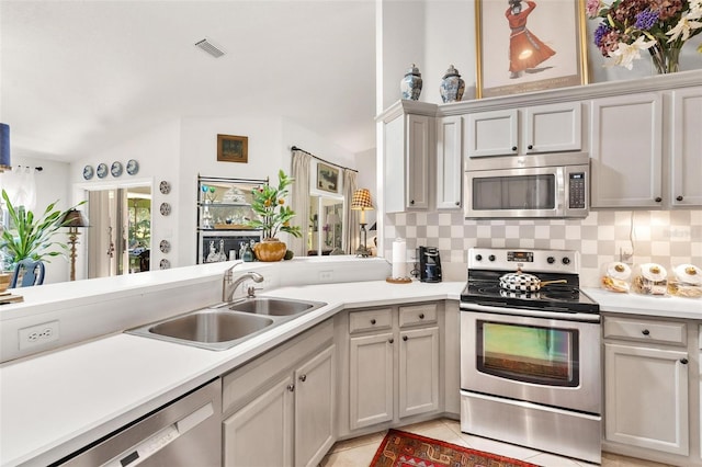 kitchen with kitchen peninsula, appliances with stainless steel finishes, tasteful backsplash, sink, and light tile patterned flooring