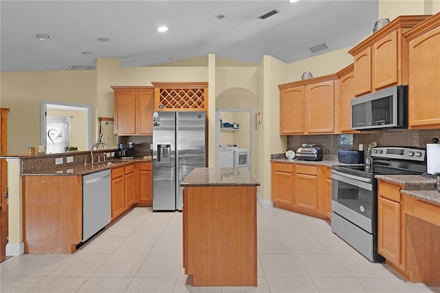 kitchen featuring stainless steel appliances, dark stone counters, lofted ceiling, decorative backsplash, and a kitchen island