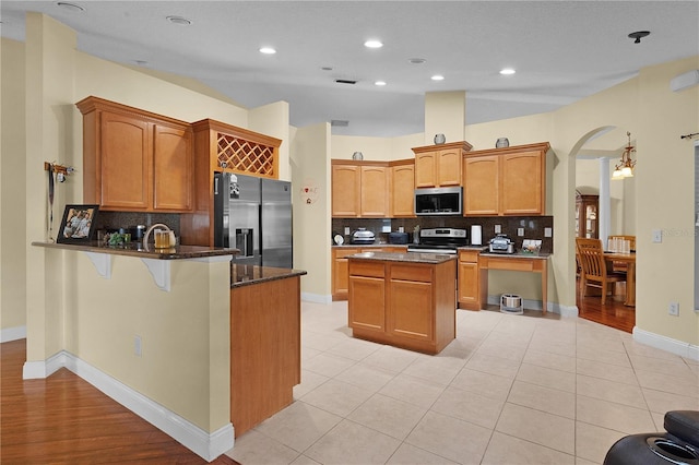 kitchen with a center island, dark stone counters, decorative backsplash, light tile patterned floors, and stainless steel appliances