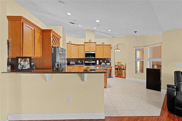 kitchen featuring a breakfast bar, vaulted ceiling, dark stone countertops, appliances with stainless steel finishes, and light hardwood / wood-style floors