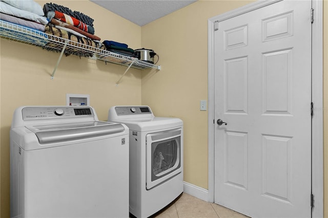 laundry room with washing machine and dryer, light tile patterned floors, and a textured ceiling