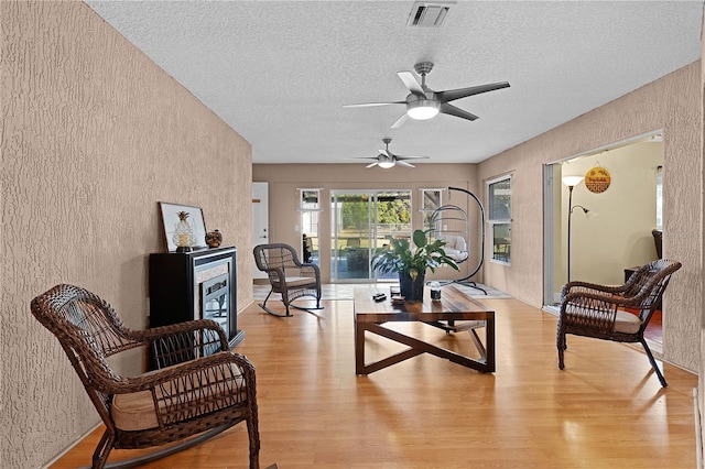 living area featuring ceiling fan, light hardwood / wood-style flooring, and a textured ceiling