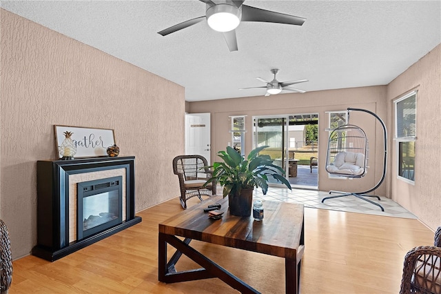 living room with ceiling fan, light wood-type flooring, and a textured ceiling