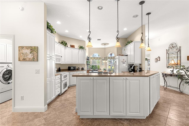 kitchen featuring white appliances, decorative light fixtures, a center island with sink, washer / dryer, and white cabinetry