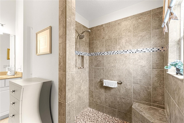 bathroom with tiled shower, a textured ceiling, and vanity