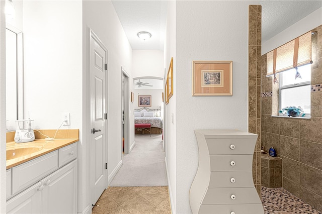 bathroom with vanity, a tile shower, a textured ceiling, and ceiling fan