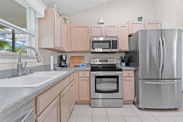 kitchen featuring stainless steel appliances, lofted ceiling, light brown cabinetry, a sink, and a textured ceiling