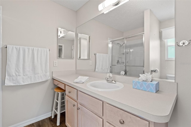 full bath with a textured ceiling, wood finished floors, vanity, baseboards, and a shower stall