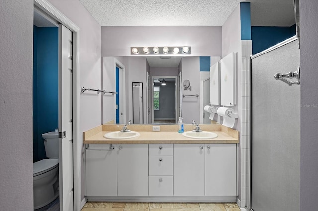 bathroom with a textured ceiling, toilet, a shower with door, and vanity