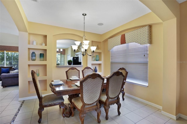 dining space with a healthy amount of sunlight, light tile patterned flooring, built in features, and an inviting chandelier