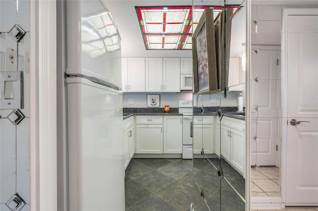 kitchen featuring white cabinets, white appliances, dark tile patterned floors, and lofted ceiling