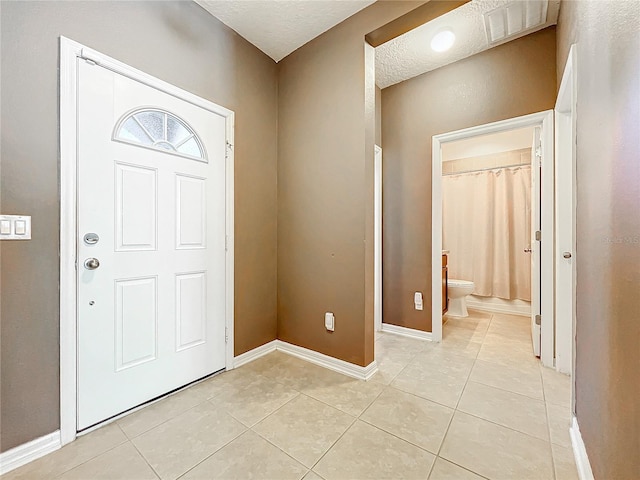 entryway with light tile patterned floors, a textured ceiling, visible vents, and baseboards