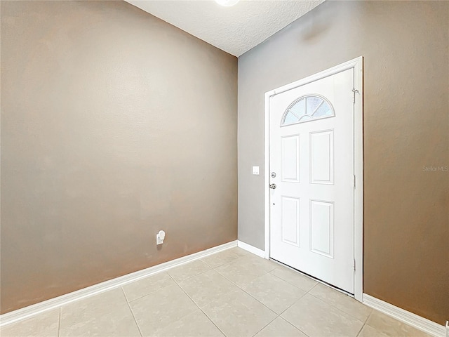 foyer entrance with light tile patterned flooring, a textured ceiling, and baseboards