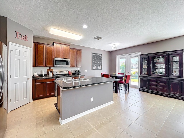 kitchen with light tile patterned flooring, stainless steel appliances, visible vents, french doors, and an island with sink