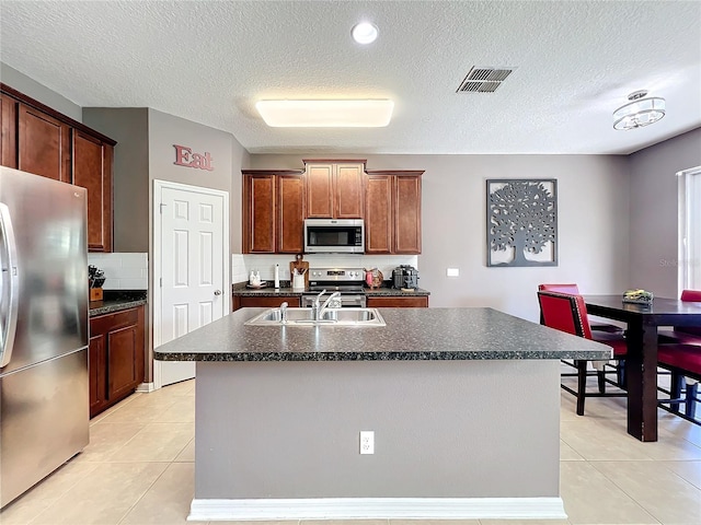 kitchen with stainless steel appliances, dark countertops, a sink, and visible vents