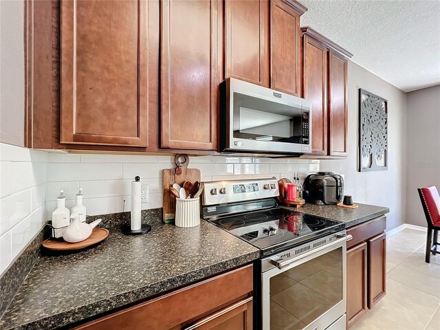 kitchen with baseboards, decorative backsplash, stainless steel appliances, a textured ceiling, and light tile patterned flooring