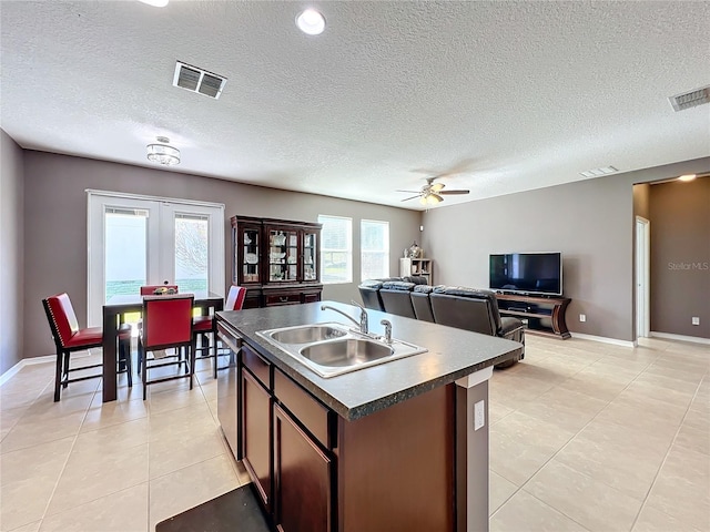 kitchen featuring dark countertops, visible vents, a sink, and an island with sink