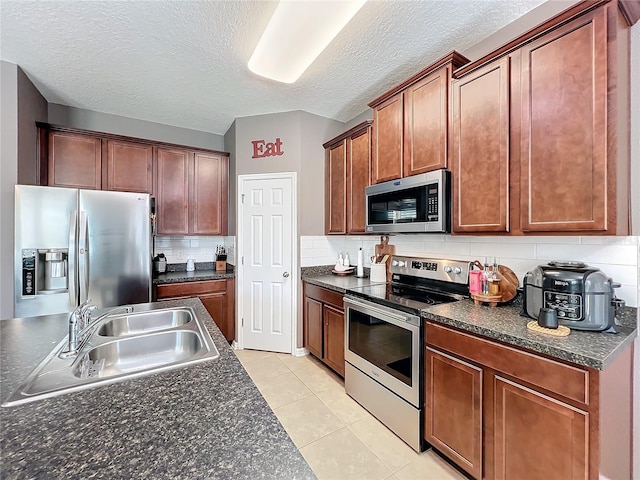 kitchen with light tile patterned floors, a sink, appliances with stainless steel finishes, decorative backsplash, and dark countertops