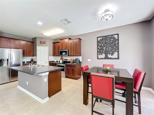 kitchen with a center island with sink, dark countertops, visible vents, appliances with stainless steel finishes, and a sink