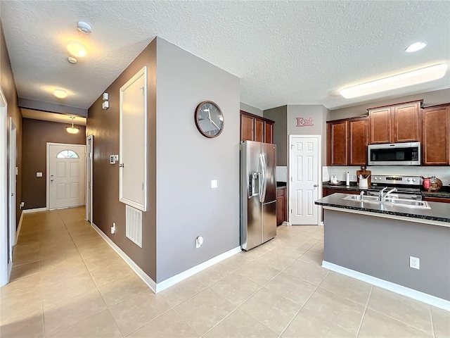 kitchen with light tile patterned floors, stainless steel appliances, a sink, a textured ceiling, and dark stone counters