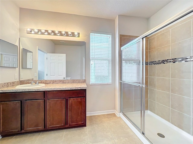 full bath with a textured ceiling, tile patterned flooring, vanity, baseboards, and a shower stall