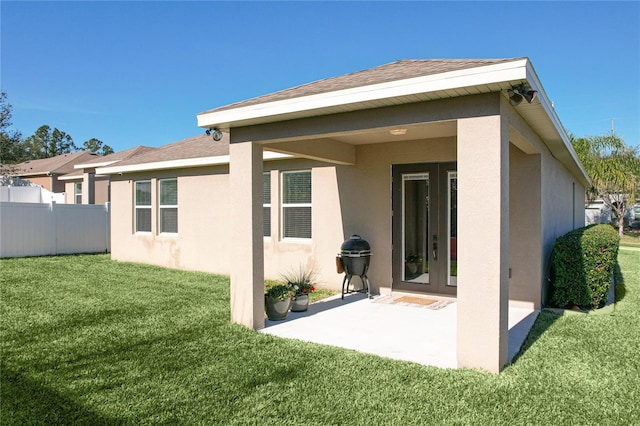 rear view of house featuring a lawn, roof with shingles, fence, french doors, and stucco siding